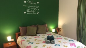 A bedroom with a green wall, a bed with a white butterfly-patterned bedspread, two pillows, a pair of rolled-up towels, and a wall quote. - Maltese Rooms (Sliema)