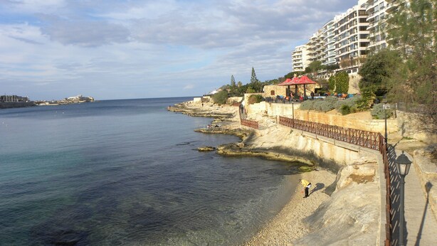 A coastal hotel with a rocky shoreline, clear blue water, and a view of the sea. - Maltese Rooms (Sliema)