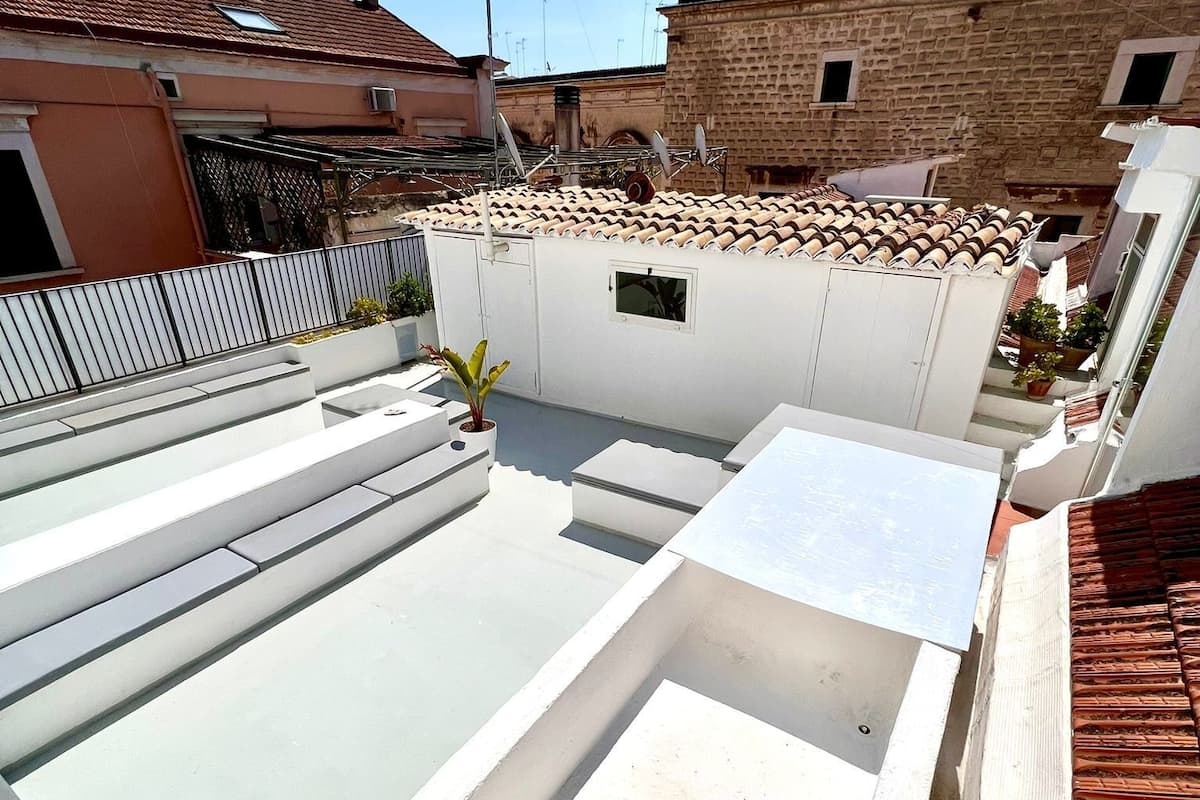 Una terraza en la azotea con piscina, paredes blancas y tejado de baldosas.