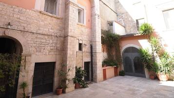 Une cour bordée de murs en pierre, dotée d’arcades et agrémentée de plantes en pot.