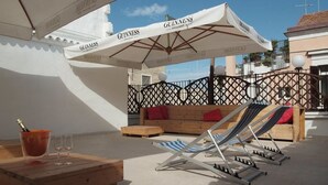 Una terraza con muebles de madera, una mesa con bebidas y vasos, y una silla de descanso bajo un paraguas GUINNESS.