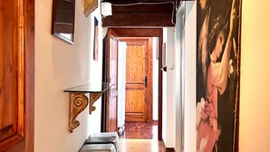 Un pasillo con piso de madera, un cuadro en la pared derecha y una puerta al final.