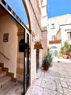 A courtyard with a stone floor, a staircase leading to an entrance, and a sign hanging from the building. - Saint Patrick B&B Guesthouse (Barletta)