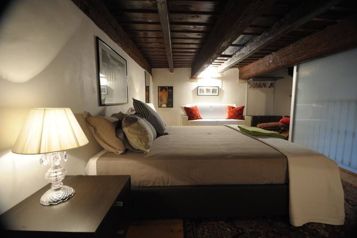 Un dormitorio con cama, una lámpara de noche, un radiador y un cuadro en la pared.