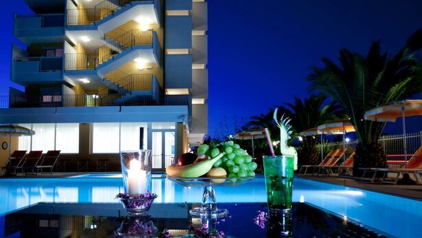 Zona de piscina con una mesa preparada para bebidas, una bandeja de frutas y una vela.