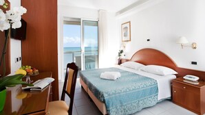 Una habitación de hotel con cama, mesita de noche, una silla, un escritorio con planta, ventana con vista y puerta.