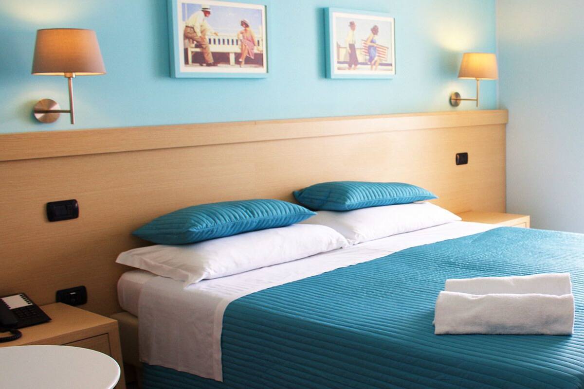 Une chambre d’hôtel avec un lit, deux lampes de chevet, une table de nuit avec un téléphone et une fenêtre avec des rideaux.