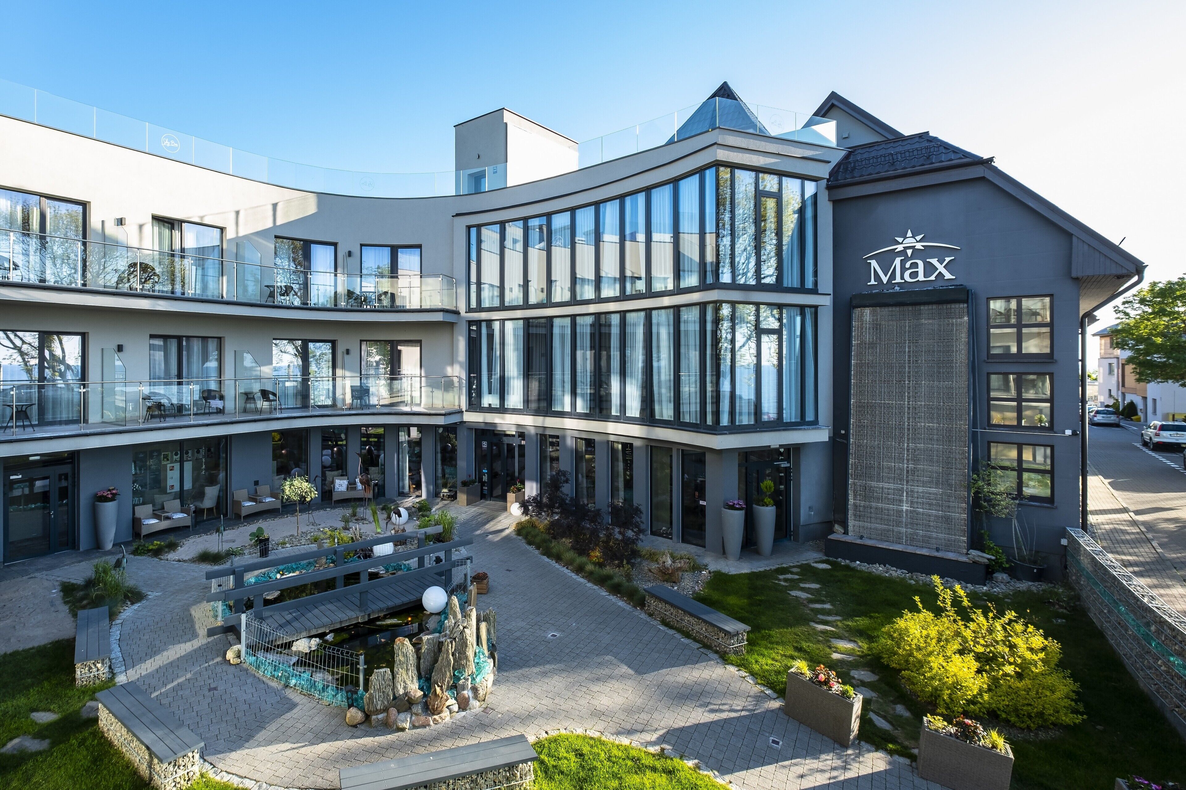Ein modernes Gebäude mit Glasfassade, einem Schild mit der Aufschrift "Max" und einem begrünten Innenhof mit Sitzgelegenheiten.
