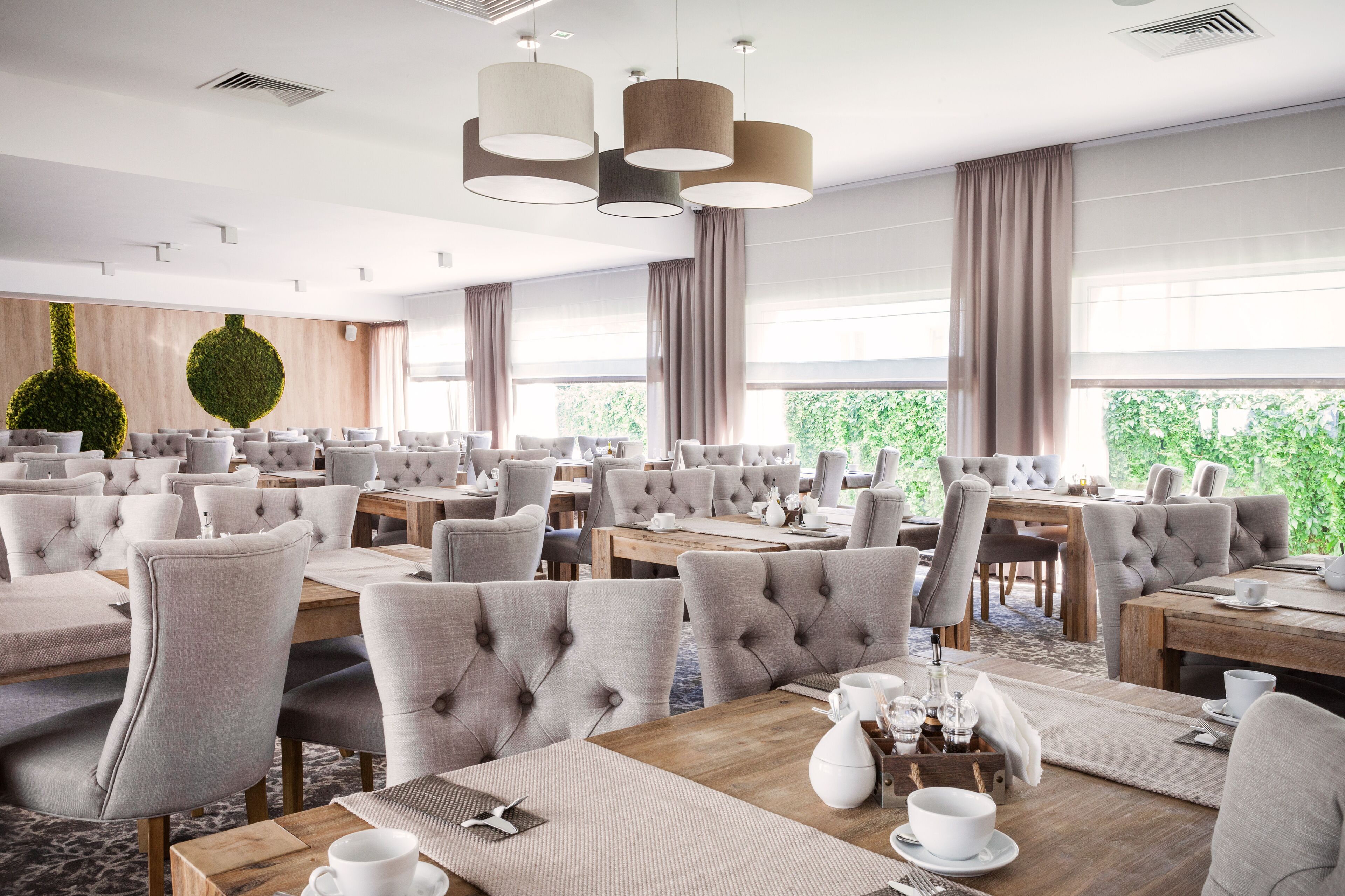 Un espace de restauration moderne, doté de plusieurs tables et chaises, de grandes fenêtres et d’un mur végétal décoratif.