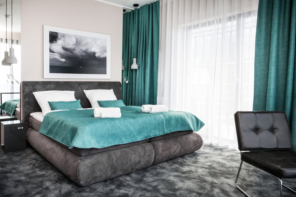 A modern bedroom with a large bed, a side table, a chair, and a window with curtains.