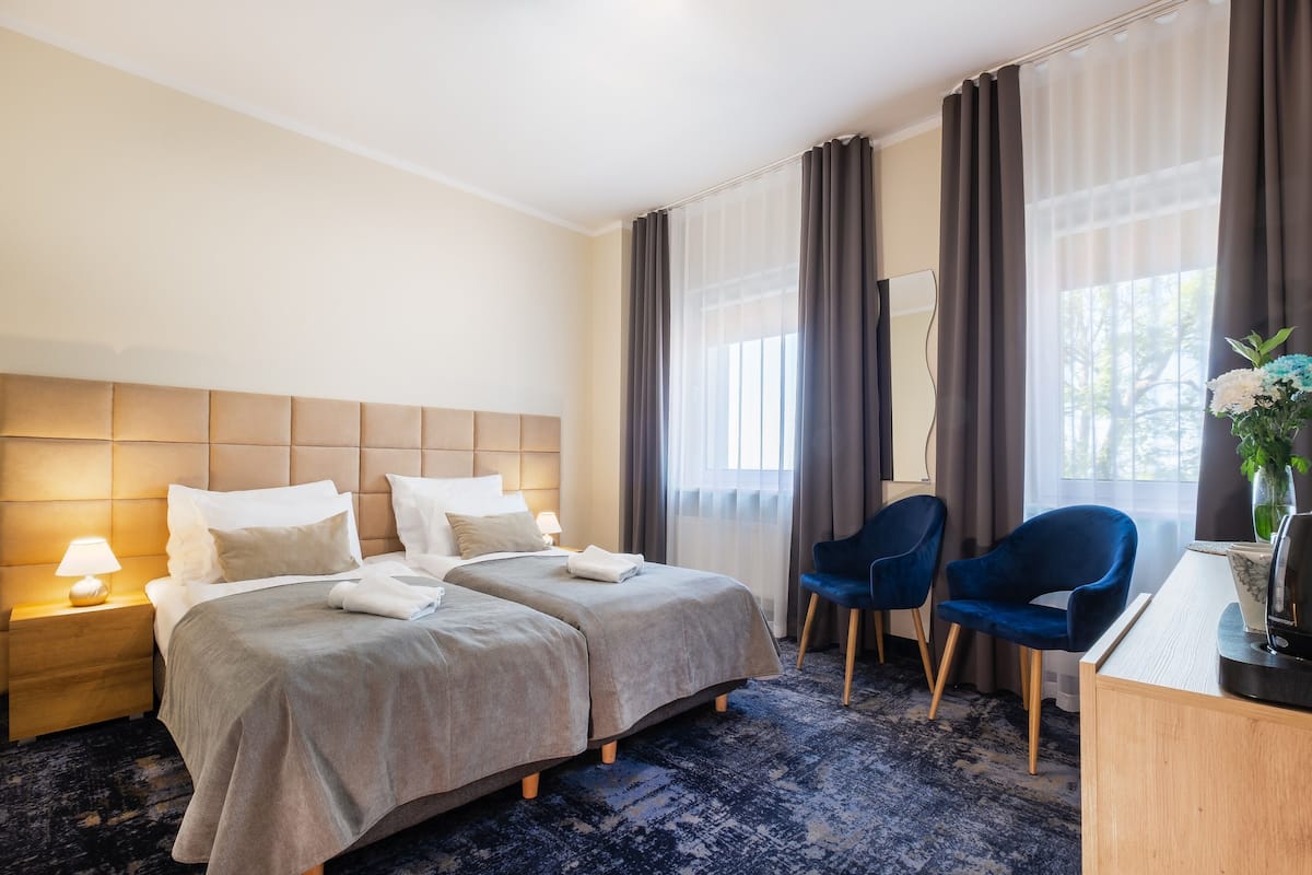 A hotel room with two beds, a desk, a chair, and a large window with curtains.