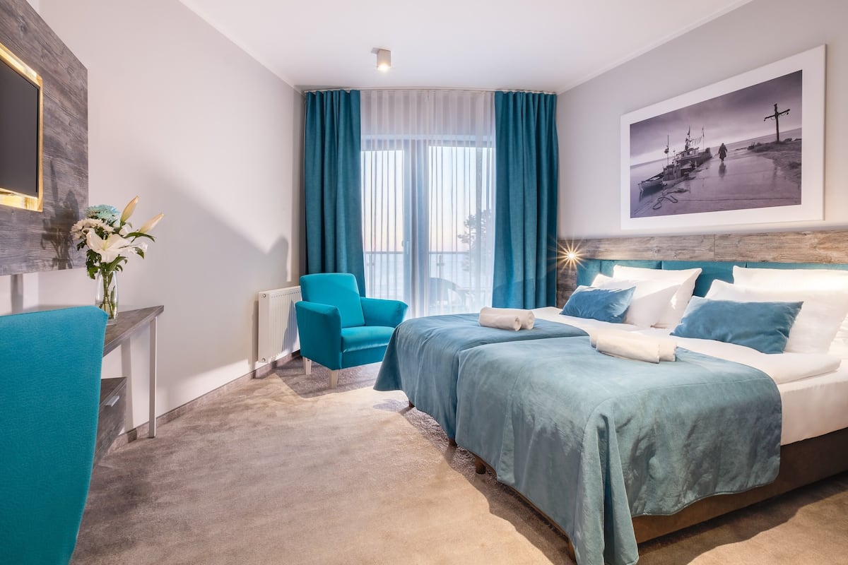 A modern hotel room with a large bed, a blue armchair, a small table, and a painting on the wall.