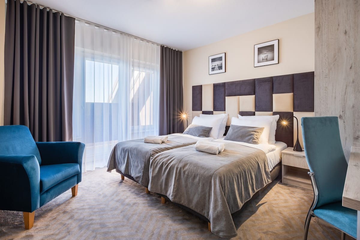 A hotel room with a large bed, two armchairs, a nightstand, and a lamp.