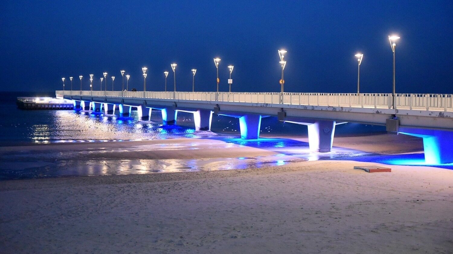 A pier with evenly spaced street lamps and a sandy beach in the foreground.