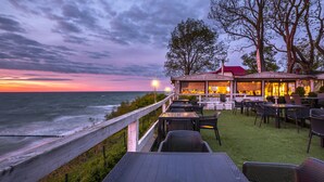 A seaside restaurant with outdoor seating overlooking the ocean, featuring a wooden deck and a view of the sunset. - Max Health Resort SPA (Ustronie Morskie)