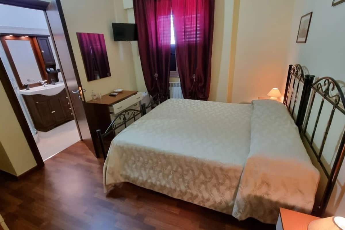 Une chambre à coucher comprenant un lit, une table de chevet, un bureau avec une chaise, un miroir et un téléviseur.