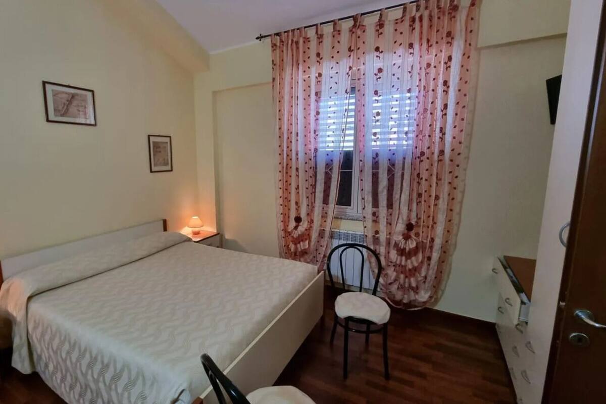 Une chambre à coucher avec un lit, des lampes de chevet, une chaise et une fenêtre avec des rideaux.
