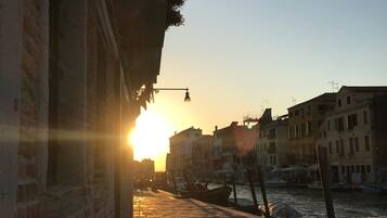 A sunset view of a canal with boats, buildings, and a cobblestone walkway.
