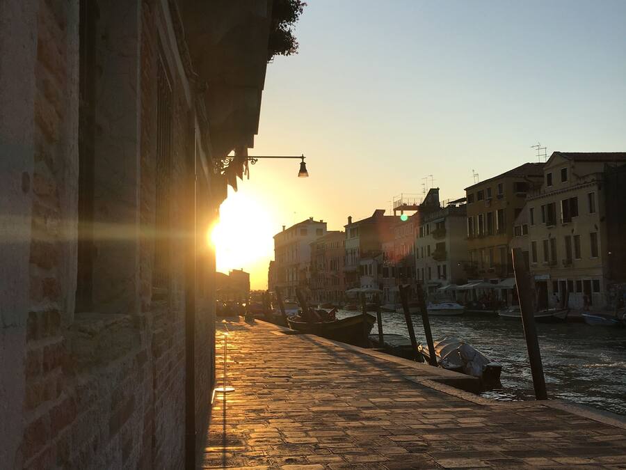A sunset view of a canal with boats, buildings, and a cobblestone walkway.