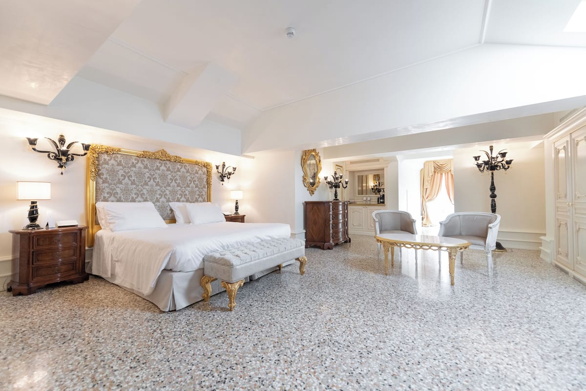 A spacious bedroom with a large bed, a sitting area with a table and chairs, and a separate dressing area with a mirror and wardrobe.