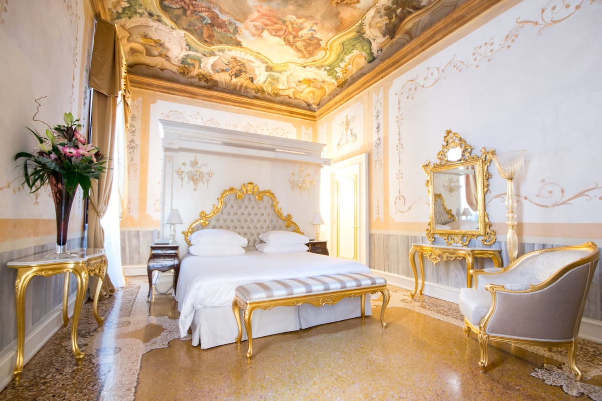 A luxurious bedroom with a large bed, ornate gold furniture, and a decorative ceiling.