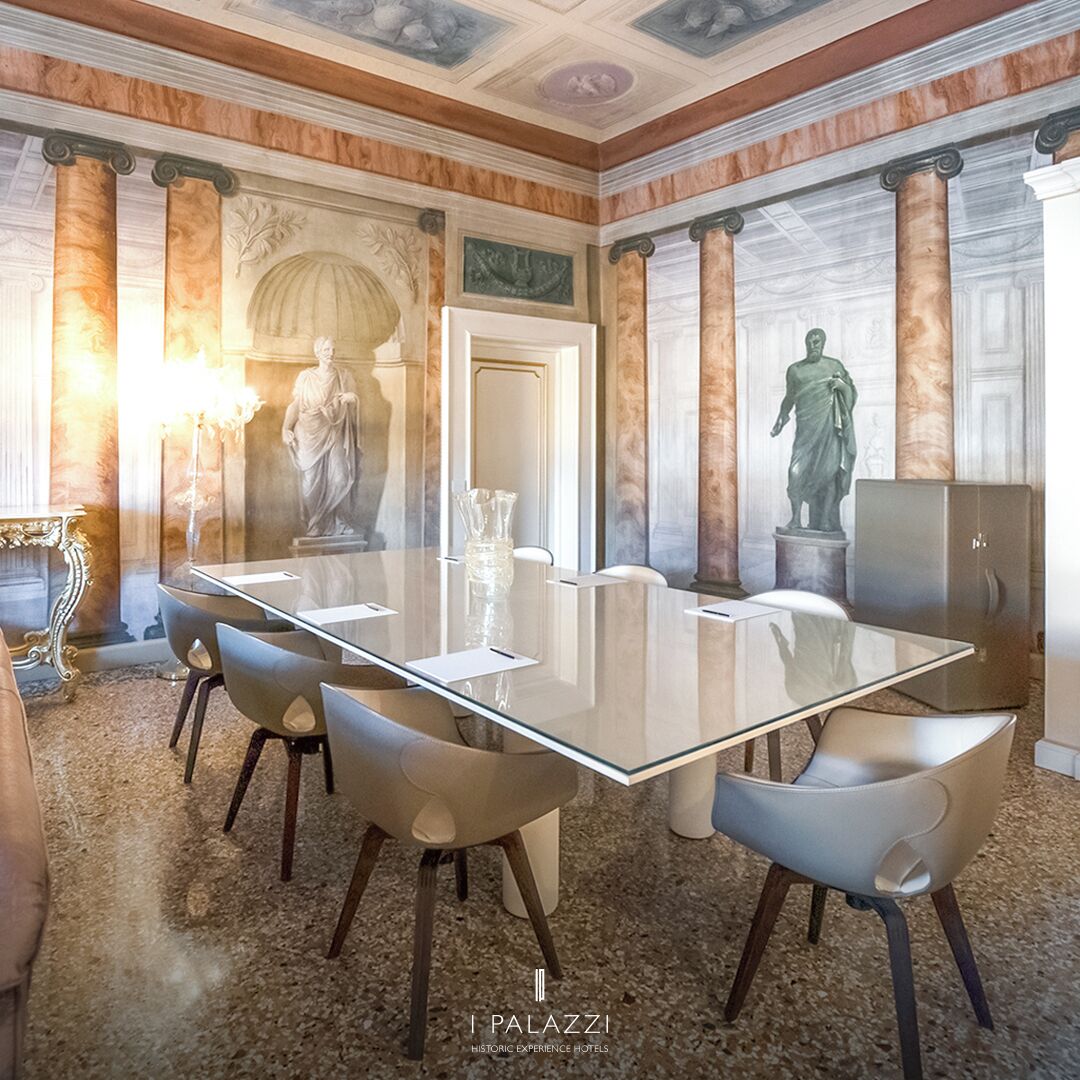 Uma sala de conferências com uma mesa de vidro, seis cadeiras e estátuas clássicas.