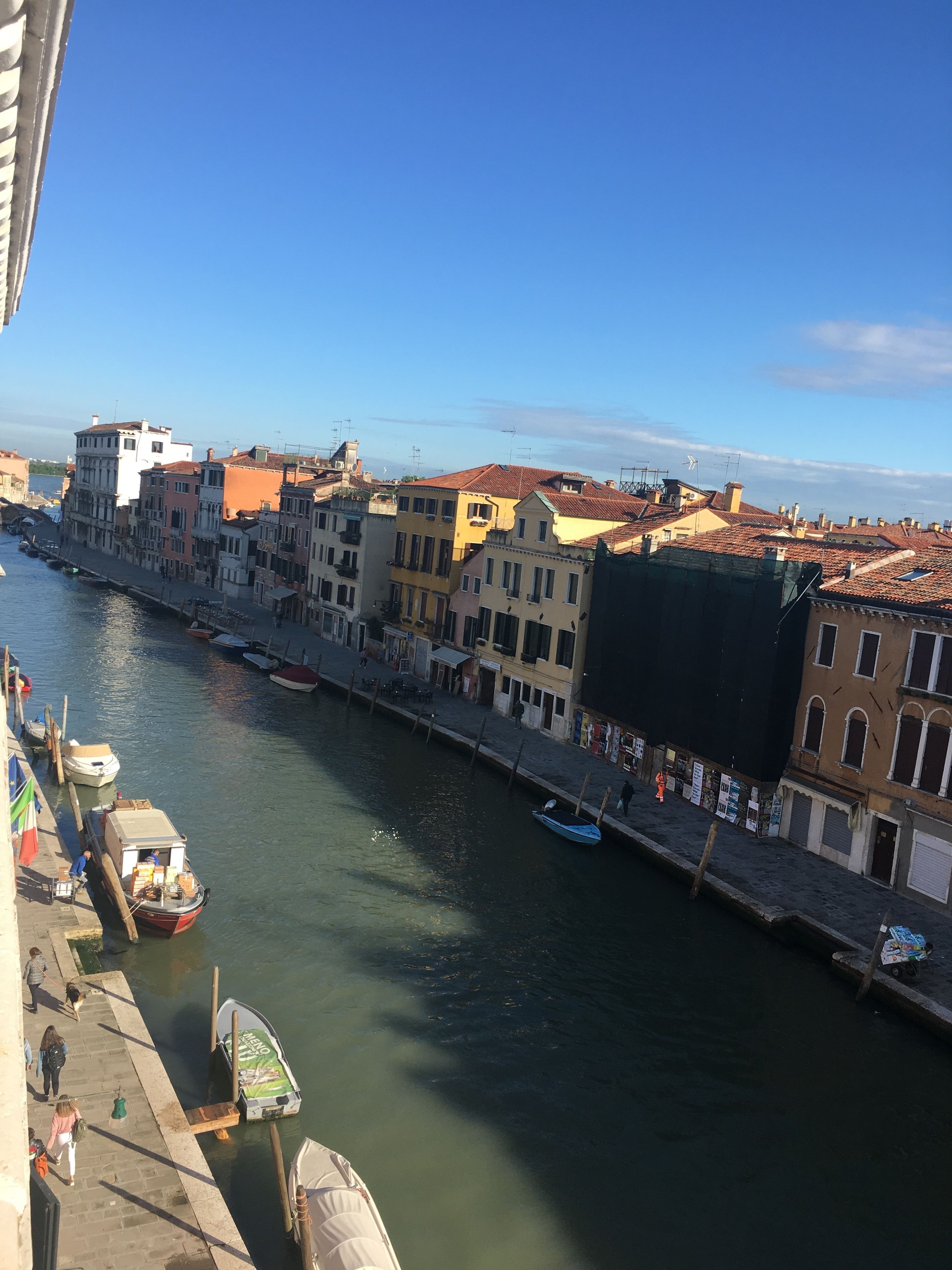 Un canal bordé d’immeubles, avec des bateaux amarrés et des gens qui se promènent sur le trottoir.