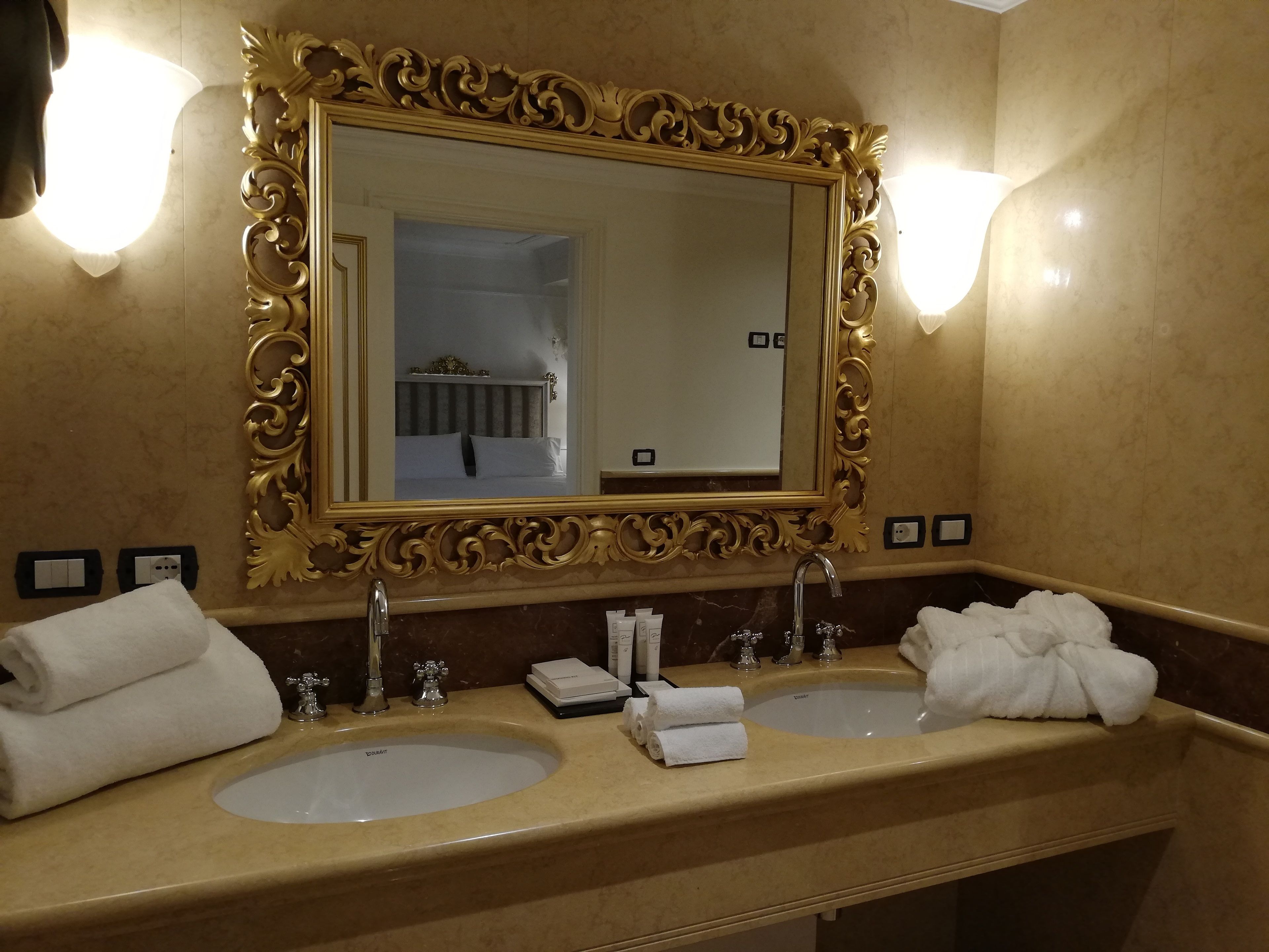 A bathroom with two sinks, a large ornate mirror, and wall sconces.
