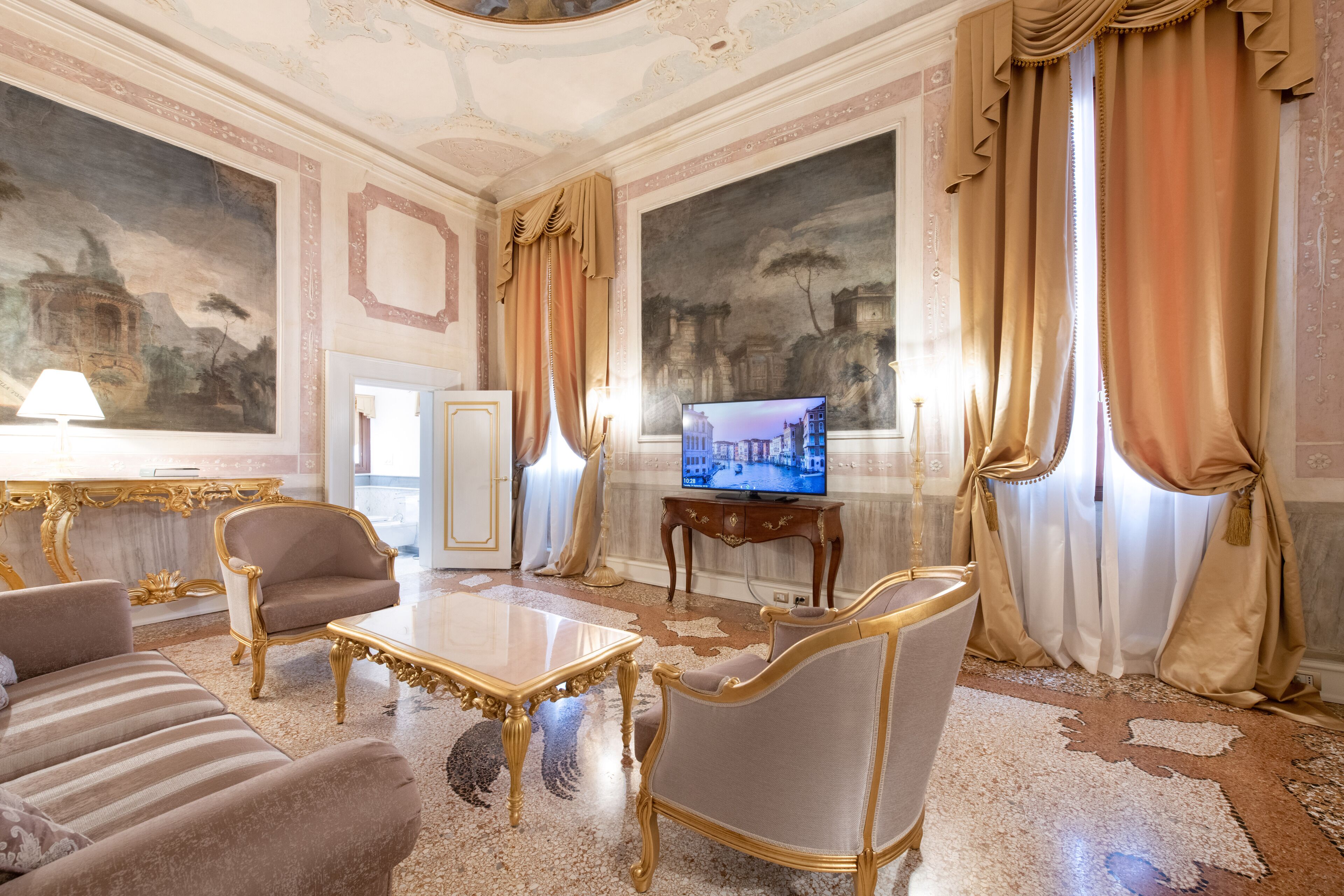 Una sala de estar lujosa con muebles ornamentados, un televisor y pinturas clásicas.