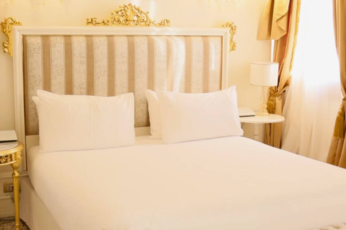 A hotel room with a large bed, two pillows, a nightstand with a lamp, and a decorative headboard.