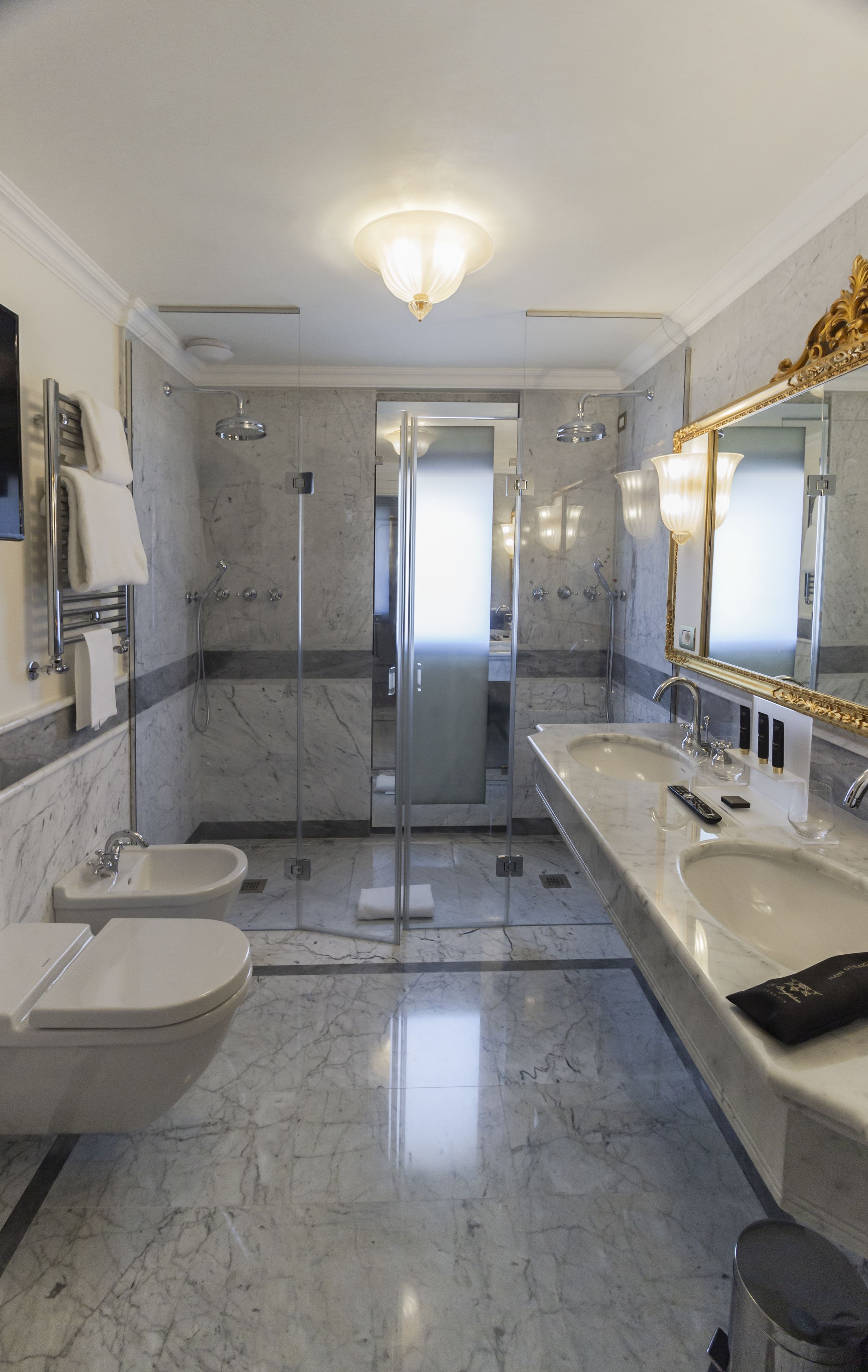 A modern bathroom with a large mirror, two sinks, a shower, and a toilet.