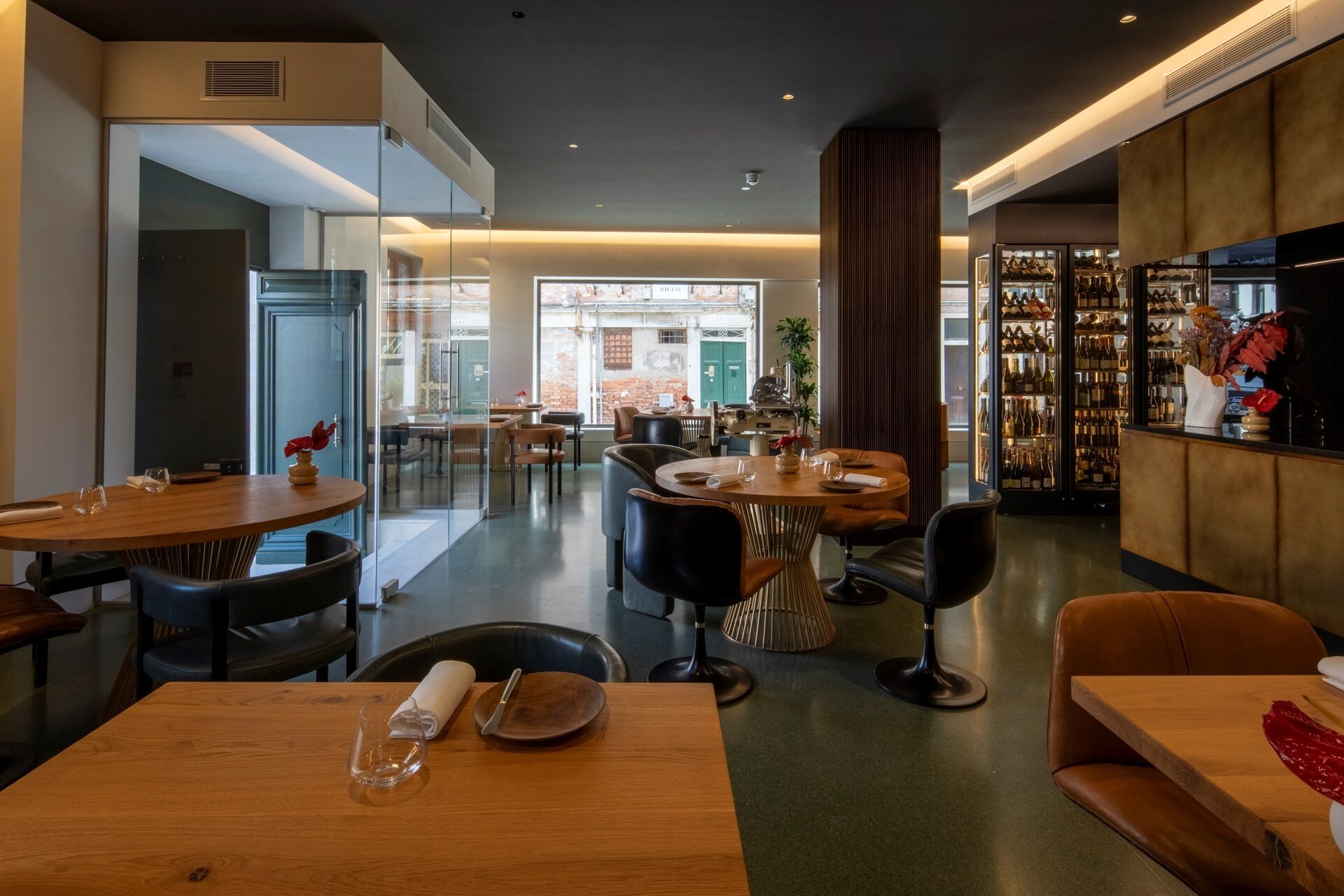 Un restaurante moderno con mesas redondas, asientos cómodos y una exhibición de vinos.