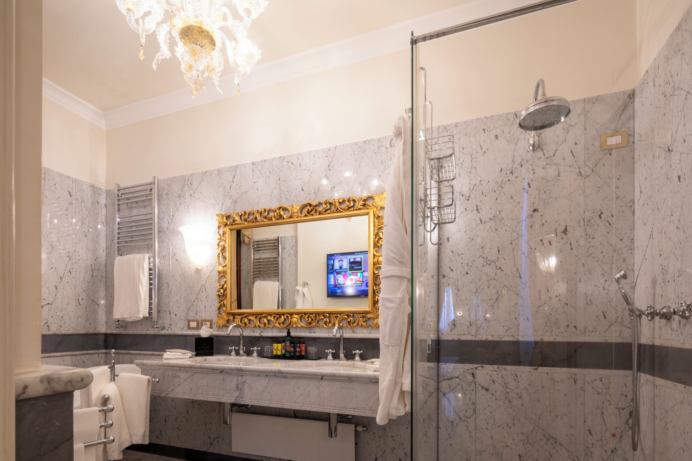 Un baño con tocador de mármol, un espejo grande con marco dorado, ducha y candelabro.