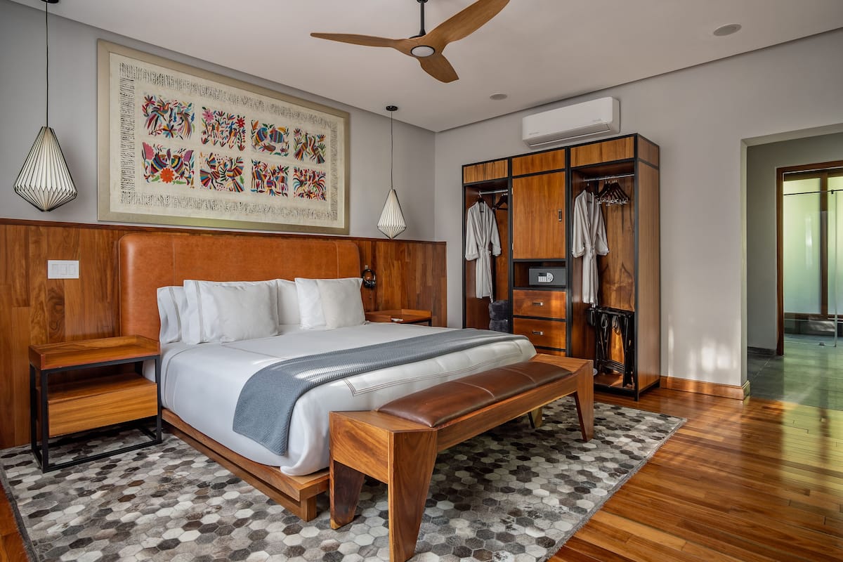 A modern bedroom with a large bed, wooden headboard, a wardrobe, and a ceiling fan.