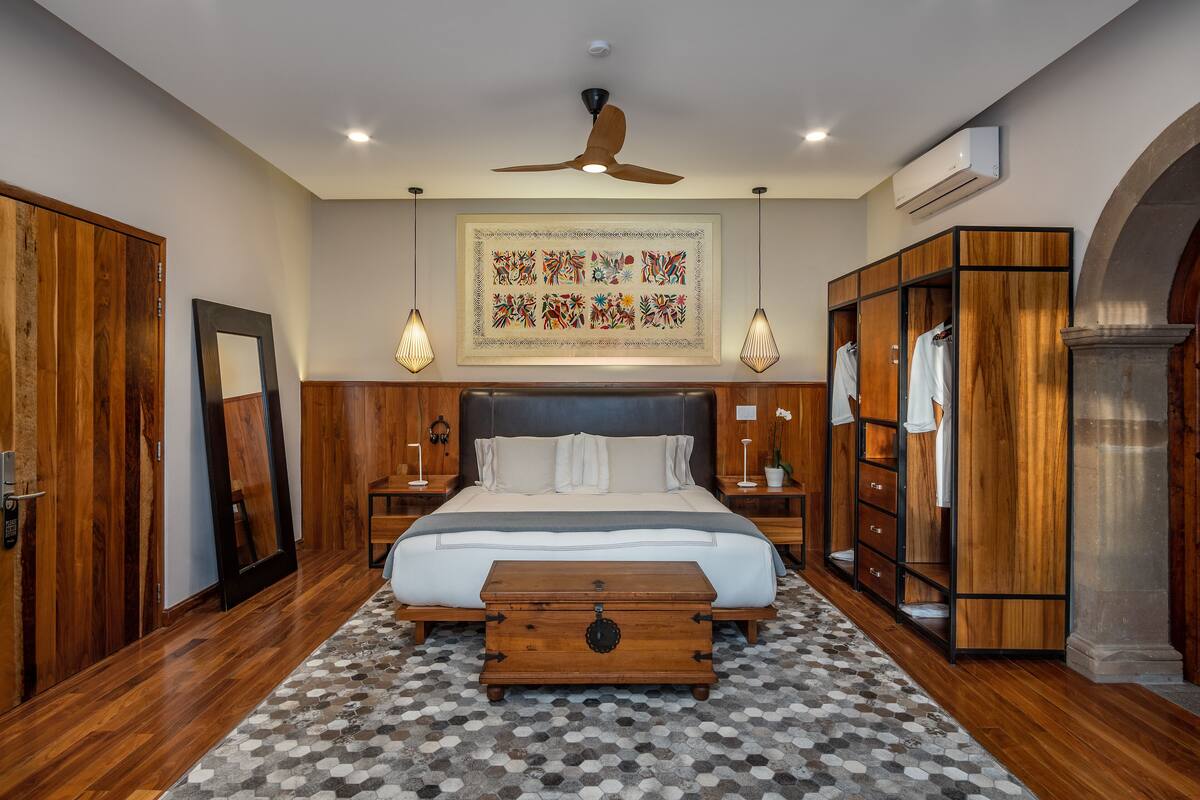 A bedroom with a large bed, wooden wardrobe, a ceiling fan, and a patterned rug.