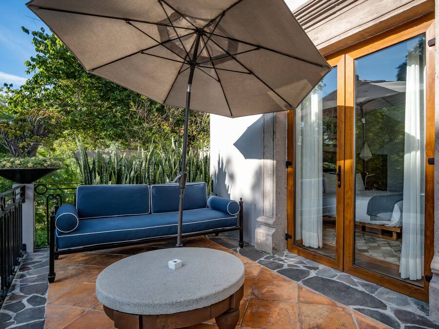 Un patio exterior con una mesa de piedra, un sofá azul y una sombrilla grande.