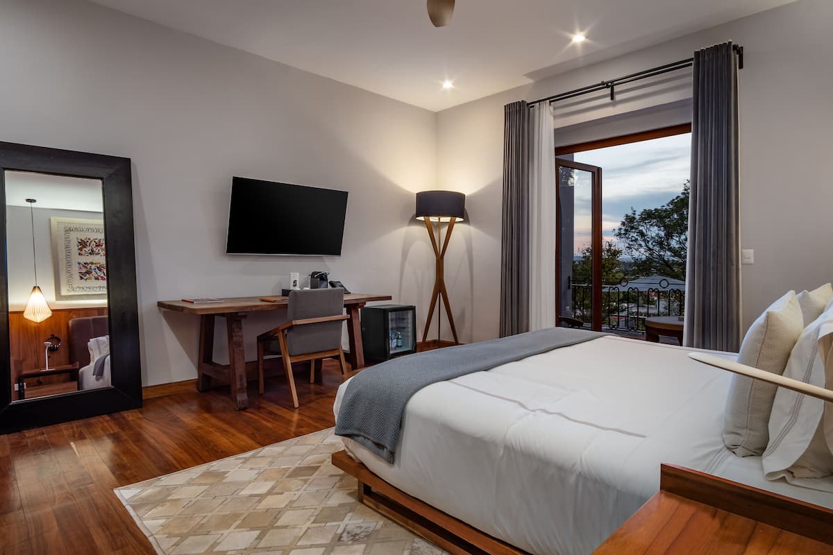 A modern hotel room with a large bed, a desk with a chair, a flat-screen TV, and a view of the outdoors.