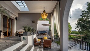 Ein überdachter Außenbereich mit Steinböden, einer Treppe zu einer oberen Ebene und einem Gartenblick durch einen Bogen.