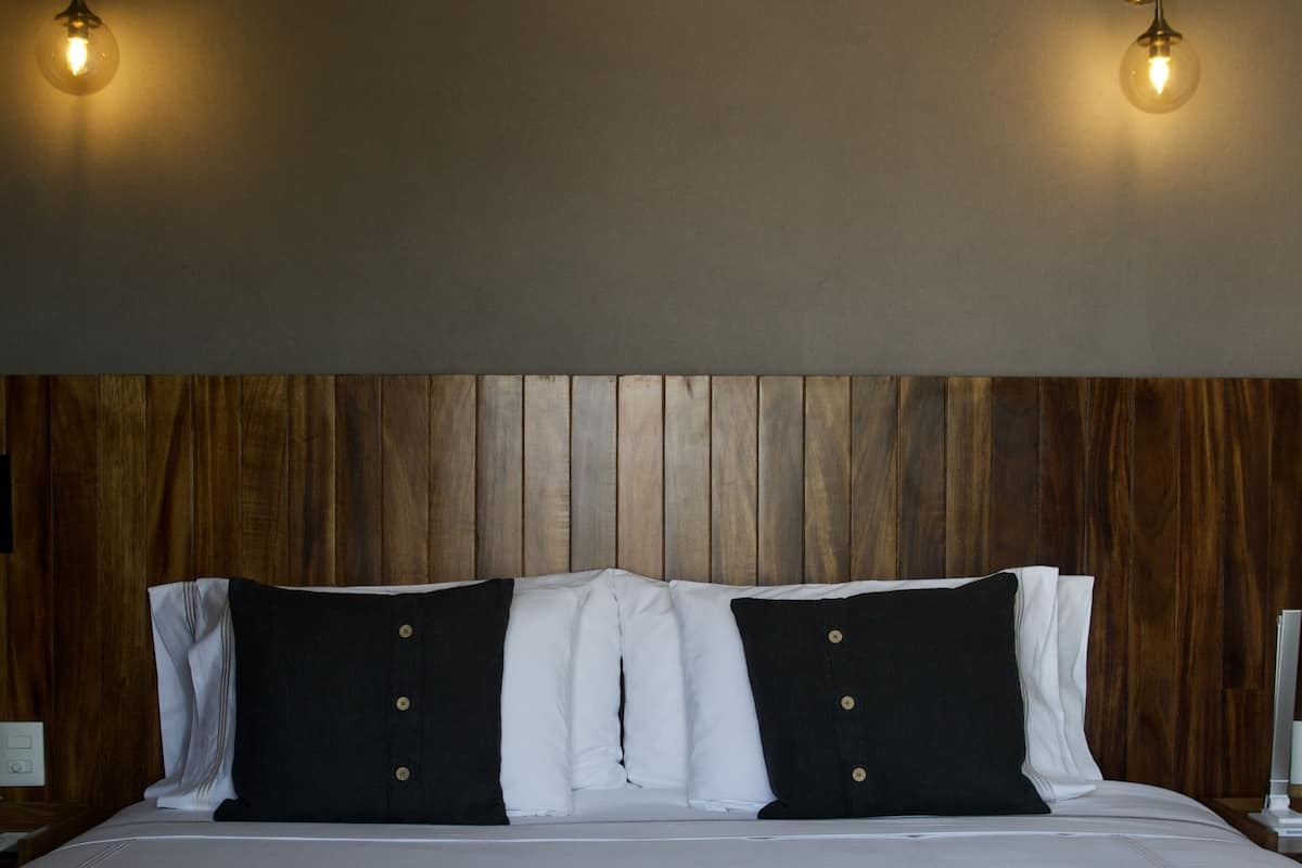 A hotel room with a wooden headboard, a large bed with white bedding and black pillows, and two wall-mounted light fixtures.