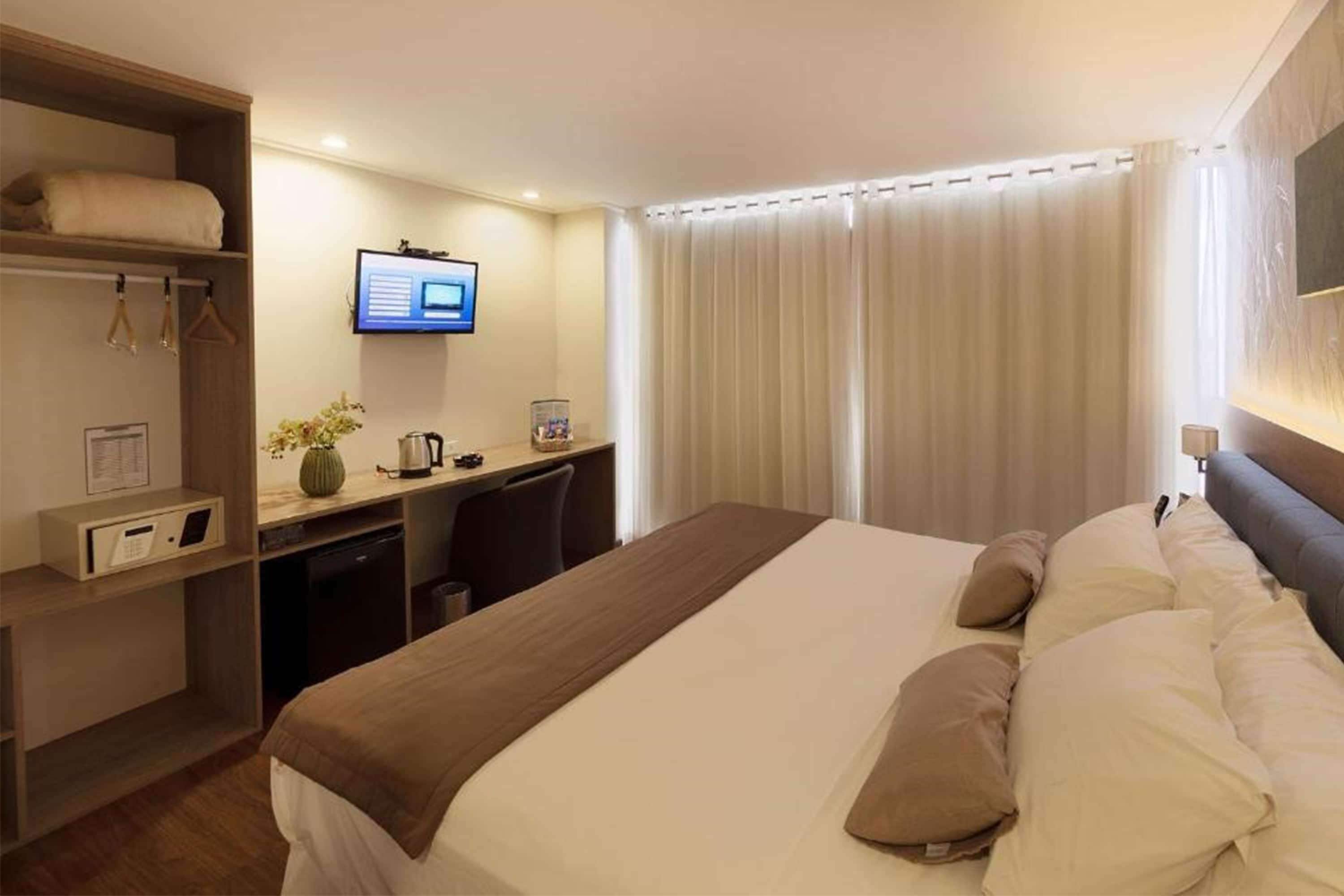 A hotel room with a bed, a desk, a television, and a window with curtains.