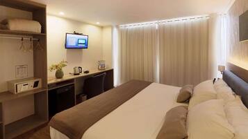 A hotel room with a bed, a desk, a television, and a window with curtains.