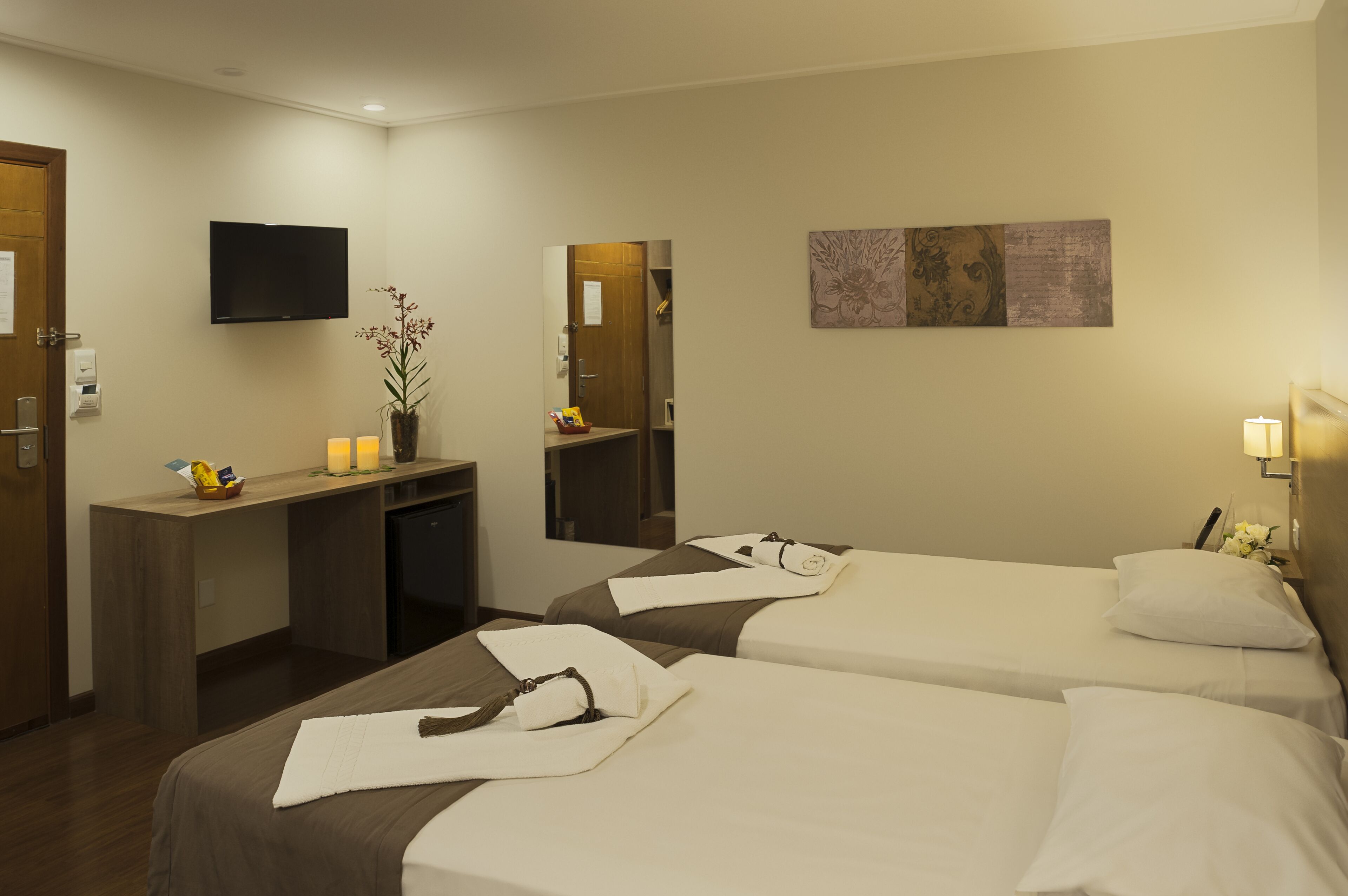 Quarto de hotel com duas camas, uma escrivaninha, uma televisão e um espelho.
