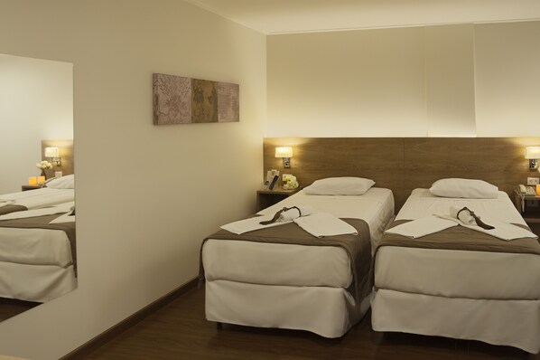 A hotel room with two beds, a wooden headboard, bedside lamps, and a mirror.