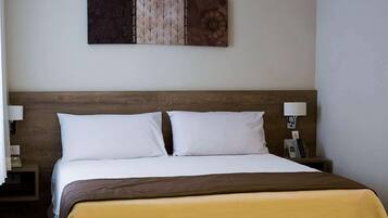 Une chambre d’hôtel avec une tête de lit en bois, deux oreillers blancs, une couvre-lit marron et une œuvre d’art accrochée au mur.