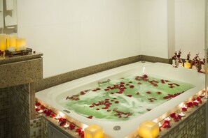 A bathtub filled with water and rose petals, surrounded by candles and flowers. - TRYP by Wyndham Varginha Cafe Royal (Varginha)