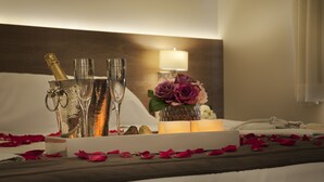 Ein Bett mit Rosenblättern, Champagnergläsern und einem Blumenstrauß.