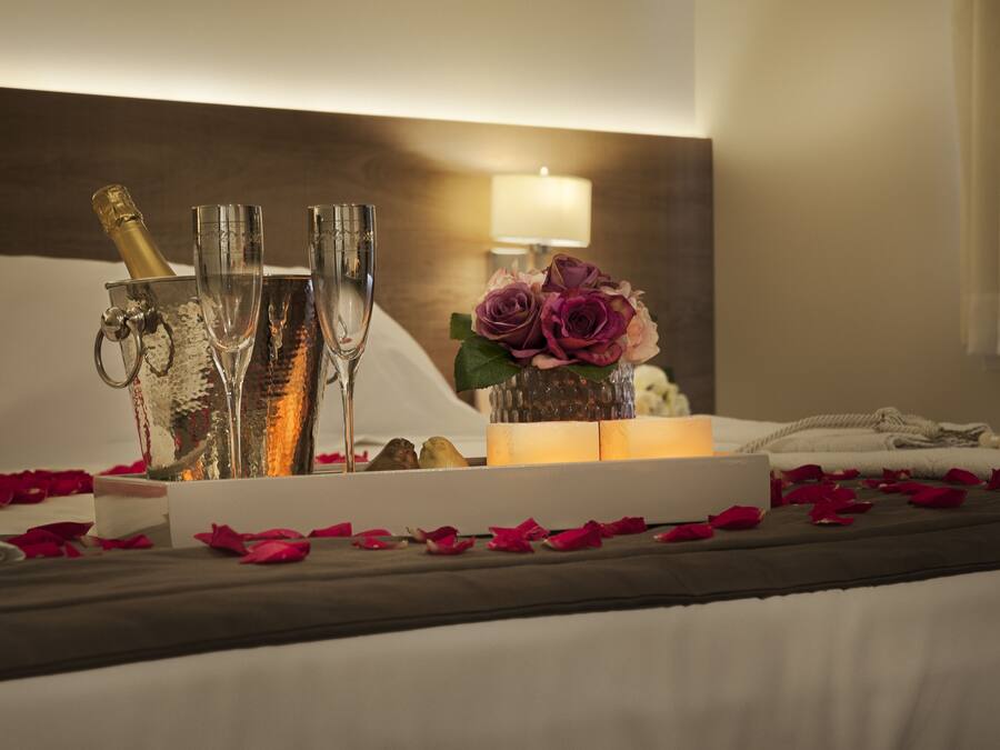 Una cama con pétalos de rosa, copas de champán y un jarrón de flores.