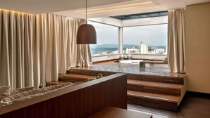 Ein modernes Interieur mit einer Holzbank, einer hängenden Leuchte und Blick auf die Stadt durch große Fenster.