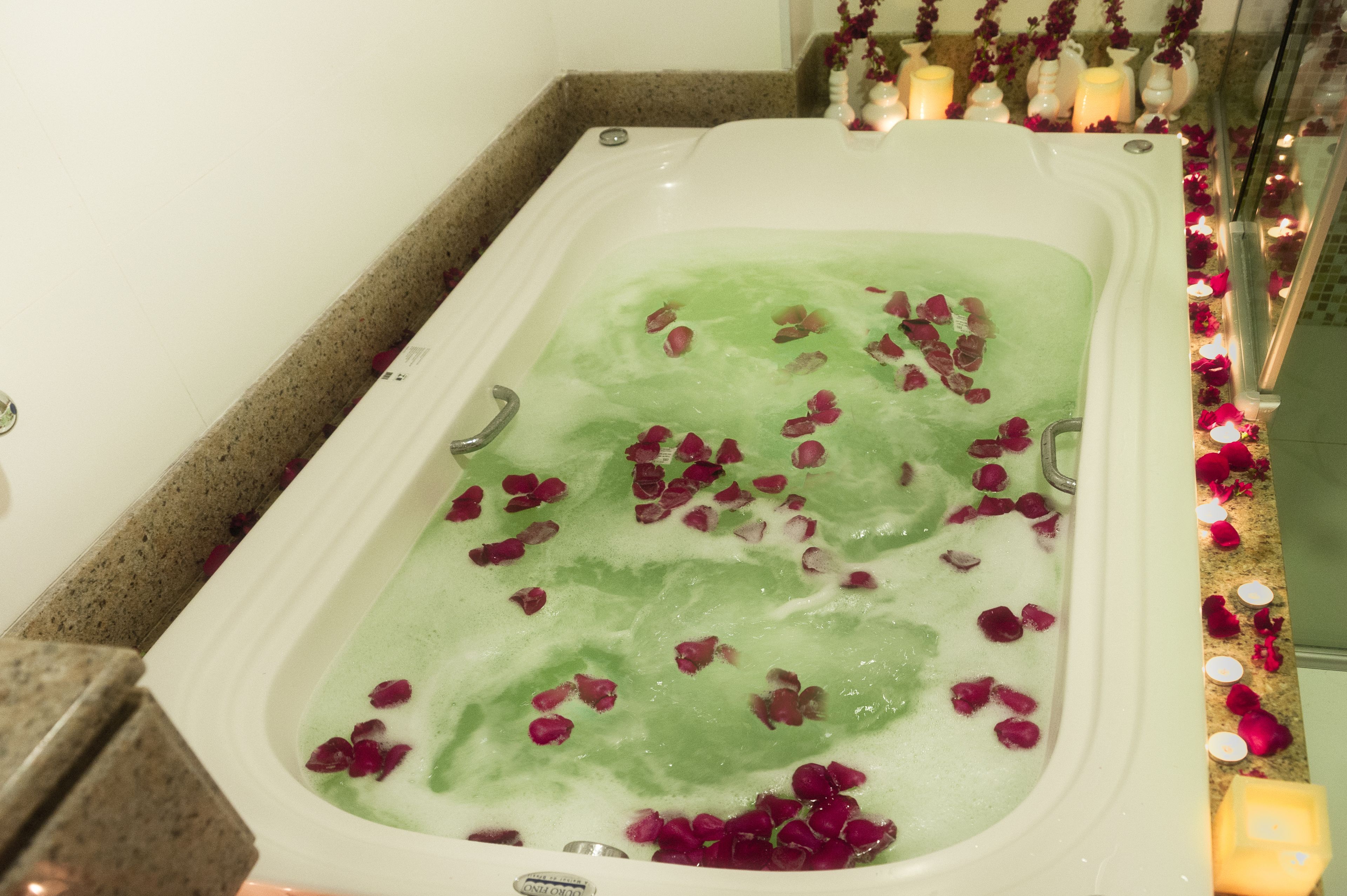A bathtub filled with green water and rose petals, surrounded by candles and flowers.