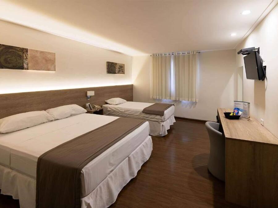 Habitación de hotel con dos camas, un escritorio, un televisor y una ventana con cortinas.